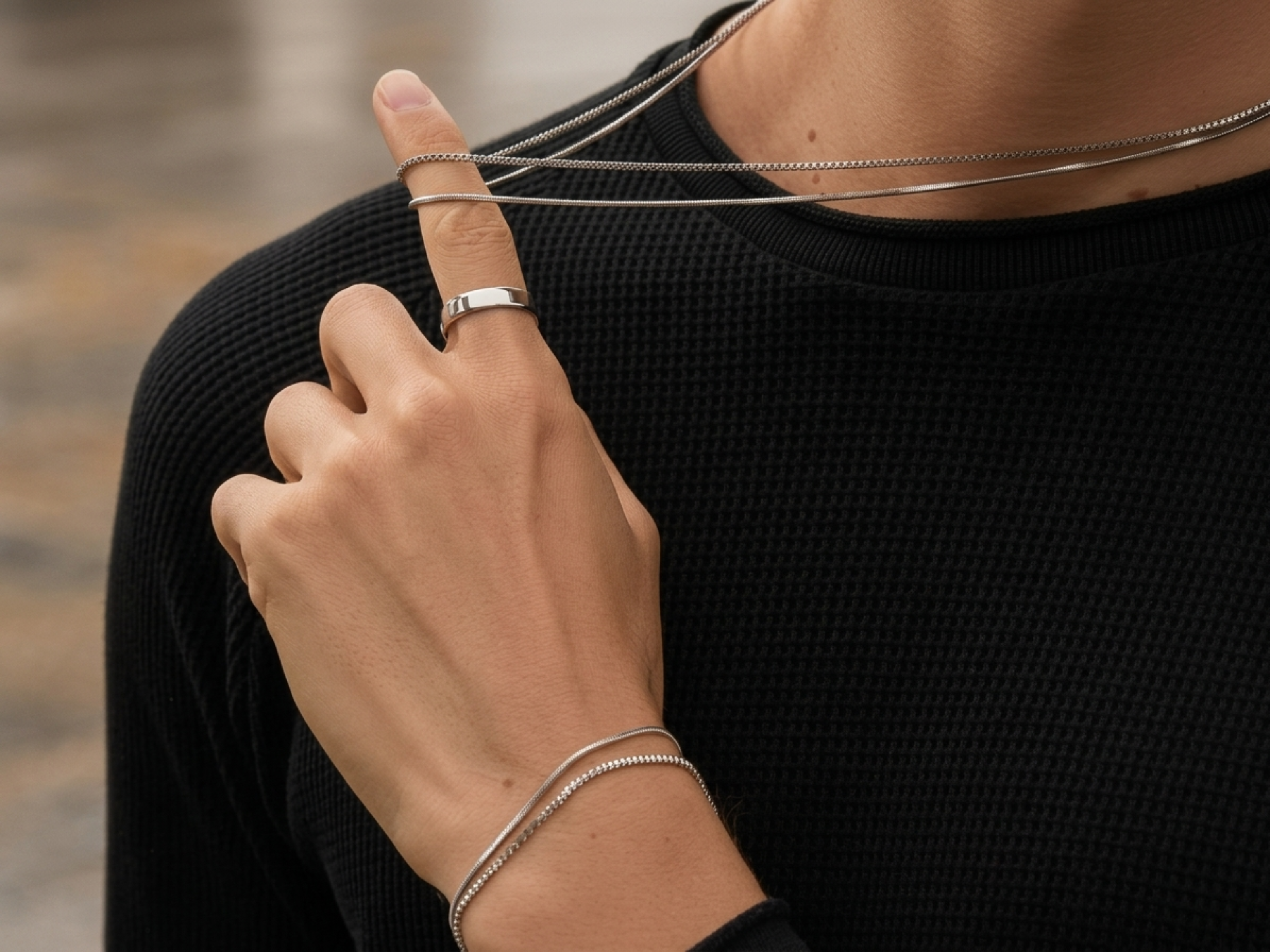 Person wearing a silver ring and bracelet on a blurred background